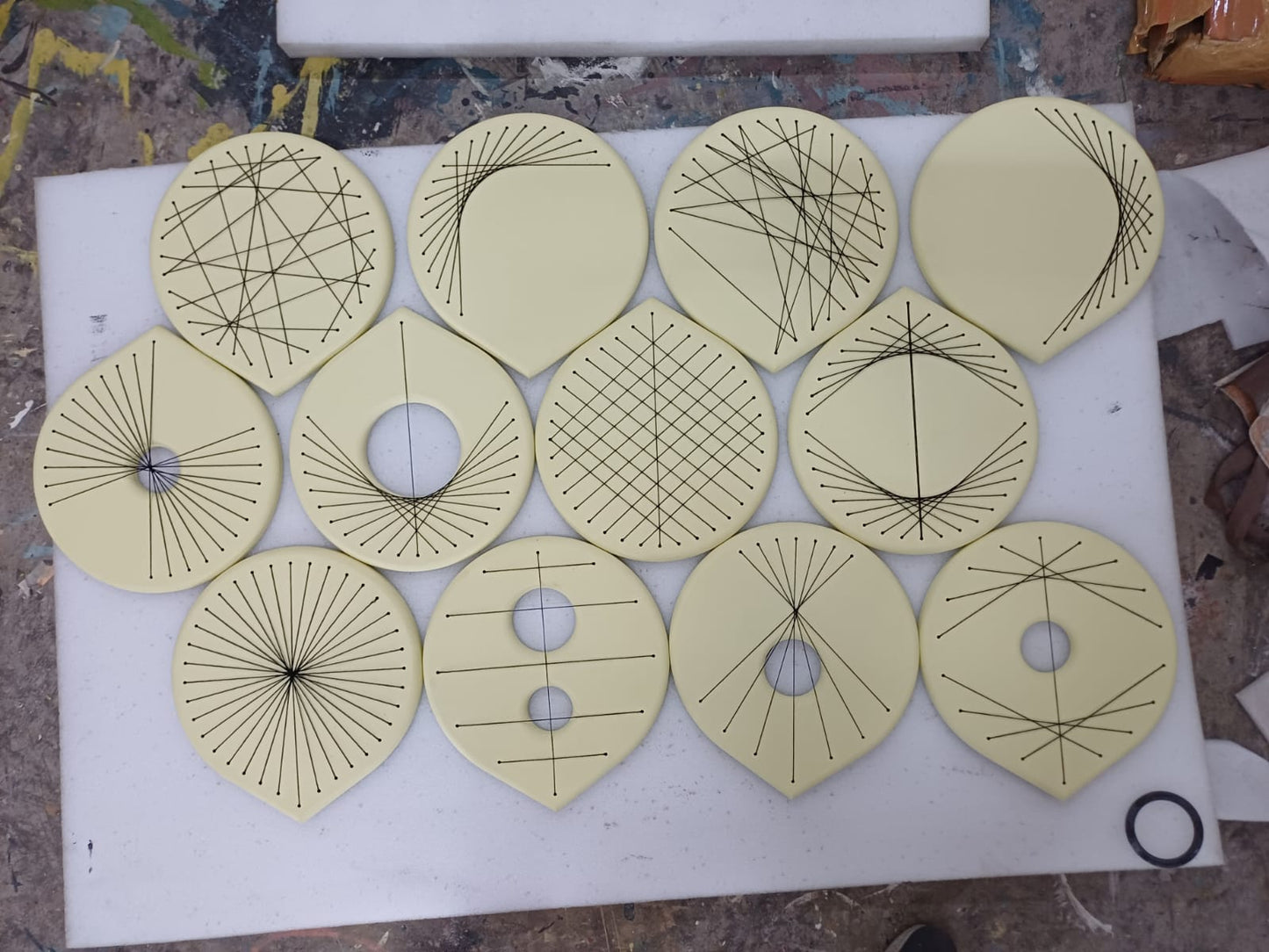 Twelve pale yellow circular or donut-shaped geometric templates with black printed lines and cutouts, arranged on a white workbench.